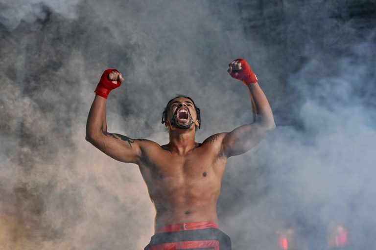 Natália Silva faz história e garante cinturão inédito para o Brasil no peso-mosca Lutadora de MMA comemora com os punhos erguidos em meio à fumaça.